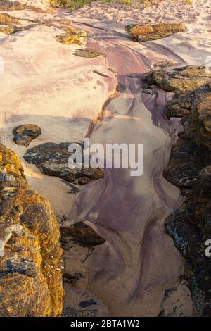 Patterns created by water flowing across sand between rocks Stock Photo
