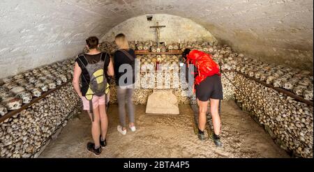 Tourists looking at the painted skulls and bones at the famous charnel house at the mountain village Hallstatt in the Salzkammergut region in Austria Stock Photo