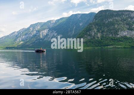 Woman crossing Lake Hallstatt on a motorboat, towing another boat, with the stunning mountain scenery of the Salzkammergut, Austria, in the background Stock Photo