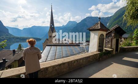 Female tourist looking at stunning Hallstatt, Salzkammergut region, OÖ, Austria, from an elevated viewing point above the roofs of the famous village Stock Photo
