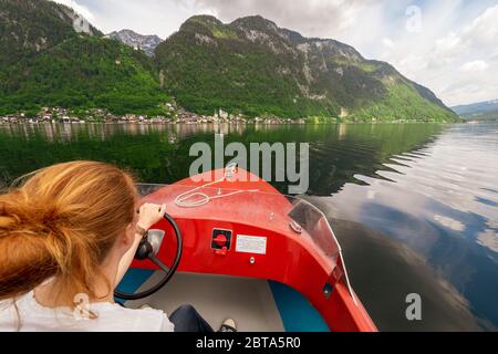 Female tourist cruising with small red boat on Lake Hallstatt in front of the waterfront of the famous town Hallstatt, Salzkammergut region, Austria Stock Photo