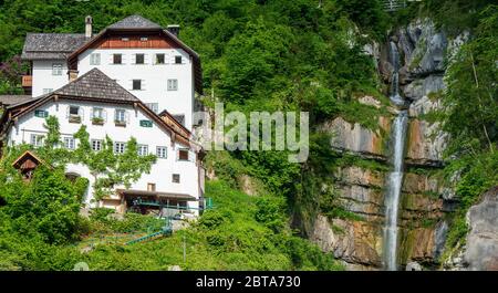 Traditional old house built high above the mountain village Hallstatt in the Salzkammergut region, OÖ, Austria, with a small waterfall splashing down Stock Photo