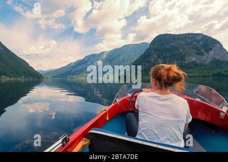 Female tourist cruising with small red boat on Lake Hallstatt in front of stunning mountain scenery near Hallstatt, Salzkammergut region, OÖ, Austria