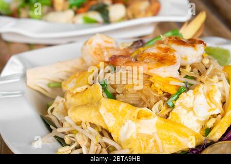 Omelet wraped Pad Thai with fresh shrimp in white dish on bamboo table, Fried white noodle. Stock Photo