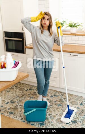 Photo of tired young woman housewife in gloves resting while mopping floor at modern kitchen Stock Photo