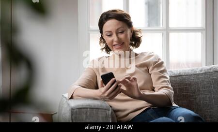 Smiling mature woman texting on smartphone at home Stock Photo