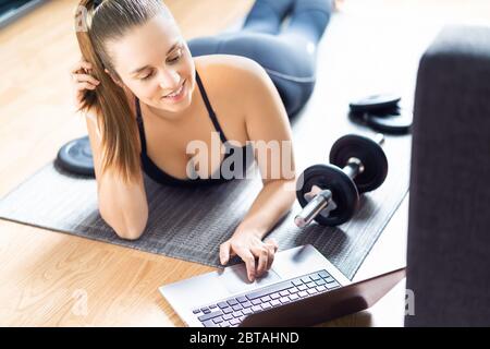 Fit woman doing home workout. Laptop computer with online gym training course. Happy fitness girl watching exercise video. Stock Photo