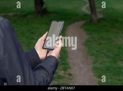 A man uses a smartphone while walking on the path at the nature. Modern technology concept. Selective focus Stock Photo