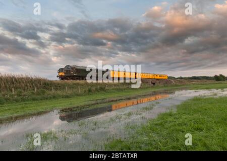 Colas class 37 locomotive 37057 in British Rail Green hauling a Network Rail infrastructure monitoring train reflected in a flooded field Stock Photo