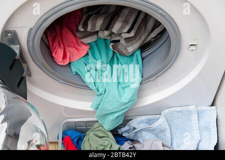 white front-loading washing machine, full of clothes. cleaning laundry. dirty laundry in the washing machine. Stock Photo