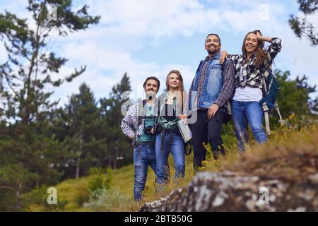 A group of tourists with backpacks are standing in the forest near the mountain. Stock Photo