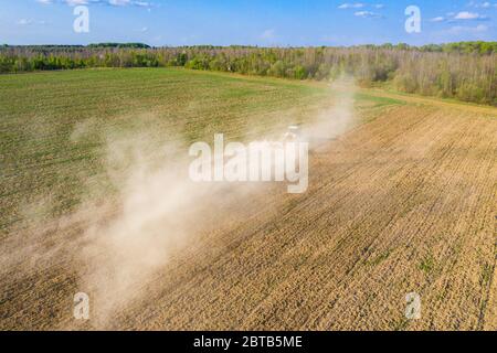 Farmer cultivates a field on a crawler tractor and loosens the soil with a disc cultivator against the backdrop of forest and blue sky 2021. Stock Photo