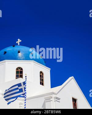 Santorini island, Greece. Greek flag waving on white orthodox church with blue dome against blue clear sky background, vertical photo Stock Photo