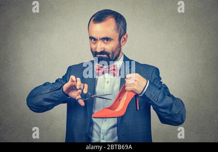 Closeup portrait middle aged man holding shoe and scissors about to cut them in studio. Mixed race bearded model isolated on grey gray gradient backgr Stock Photo