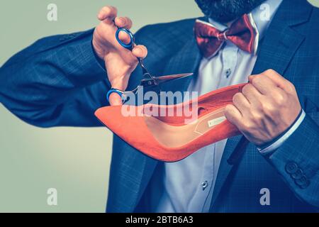 Closeup portrait middle aged man holding shoe and scissors about to cut them in studio. Mixed race bearded model isolated on green yellow gradient bac Stock Photo