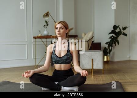 Pretty woman practices yoga on a home interior background. Relaxation and meditation in lotus position. Stock Photo
