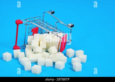An overturned shopping basket with scattered cubes of refined sugar on a blue background Stock Photo