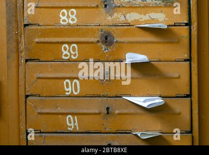 Old mailboxes in the entrance hall of a residential house filled with white paper flyers. Mass mailing concept Stock Photo