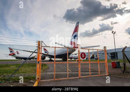 Seen through a wire fence, British Airways aeroplanes are parked at Cardiff Airport whilst unused during the Covid-19 crises. Stock Photo