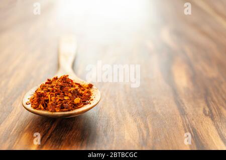 Crushed hot red cayenne peppers on a wooden spoon. Horizontal photo with plenty of empty space. Stock Photo