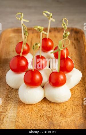 Food snacks and appetizers for buffet. Canapes with mozzarella cheese and cherry tomatoes served on wooden tray. Stock Photo
