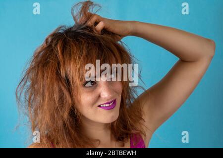 Worried young woman with frizzy red hair scratching her scalp Stock Photo