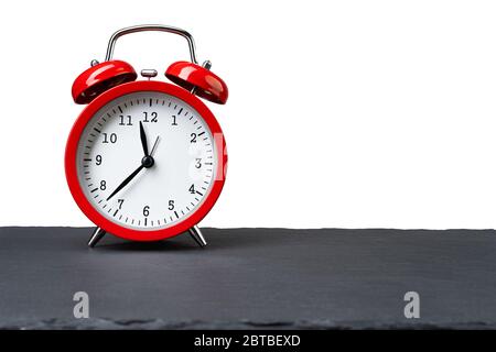 Vintage red alarm clock on dark slate plate isolated on white background. Copy space on the right. Stock Photo