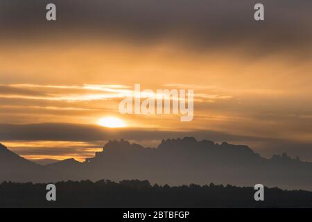 Sunset landscape showing Montserrat mountain silhouette under the sun partially covered by clouds Stock Photo