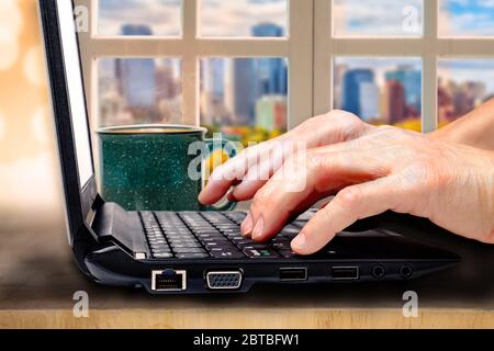 Close up of working from home concept in the new normal after Covid-19 showing fingers on computer laptop keyboard and coffee on table with vintage li Stock Photo