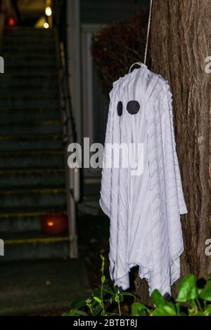 white ghost hanging on a tree during a holiday for Halloween on dark background. Stock Photo