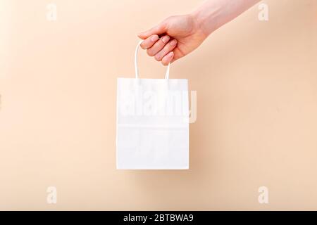 White paper shopping bag in female hand on beige light color background. Delivery, shopping, sale gift concept. Mockup bag packages. copy space for Stock Photo
