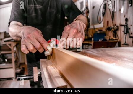 a male carpenter working in atelier, planing a wood piece with a double hand push woodworking bird planer, closeup. Stock Photo