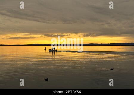 Scenic view of the lake with the silhouettes a little fishing boat and the coastline in the background at sunset, Lake Garda, Verona, Veneto, Italy Stock Photo