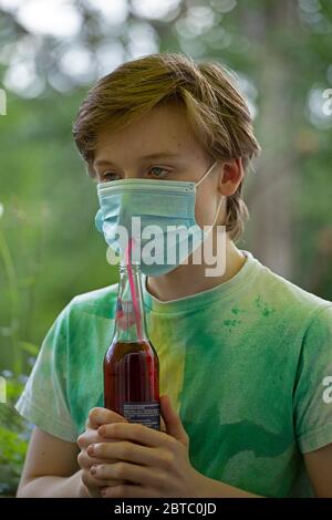 boy wearing breathing mask drinking from a bottle using a straw, Germany Stock Photo