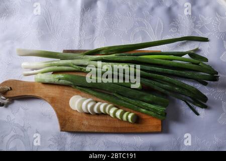 Young onion stalks and pieces of chopped onion on a wooden kitchen board at home on white background. Seasonal vegetable food concept Stock Photo