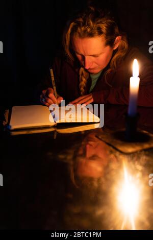 A woman writers in a journal by candlelight Stock Photo