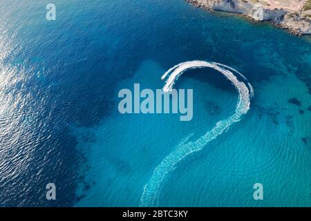 Jet ski rides in bay leaving white trail of foam on blue smooth sea surface aerial view. Stock Photo