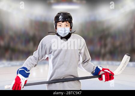 Junior ice hockey player with full equipment and sports uniform posing in fictitious arena with face mask. Concept of new normal in sports to prevent Stock Photo