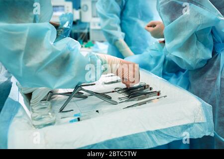 Sterile instruments on the operating table, a team of doctors lays out the instruments for the operation. many hands are brewing in sterile gloves. Stock Photo