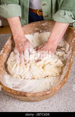 Woman kneading dough in a dough trough until it is smooth and elastic, as part of making sprouted wheat bread.  This hand-carved, antique bread or dou Stock Photo