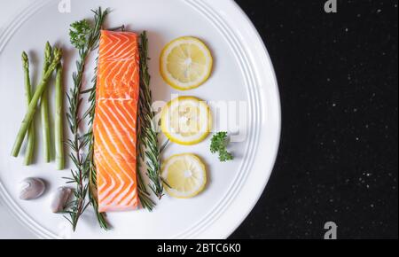 Raw fresh salmon fillet with herbs and ingredients, on white dish Stock Photo