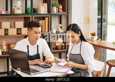 Young cafe owners sitting at table, checking bills and paying online Stock Photo