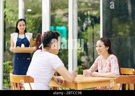 Asian young couple having sitting at cafe table and waiting for breakfast they ordered Stock Photo