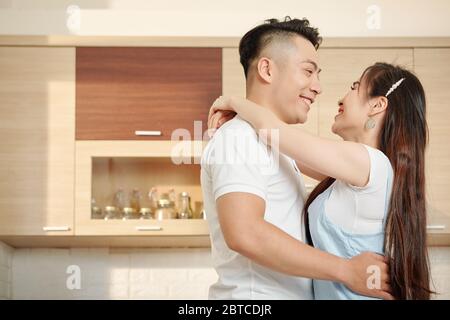 Handsome young Vietnamese man looking at his beautiful wife when they are dancing in kitchen Stock Photo