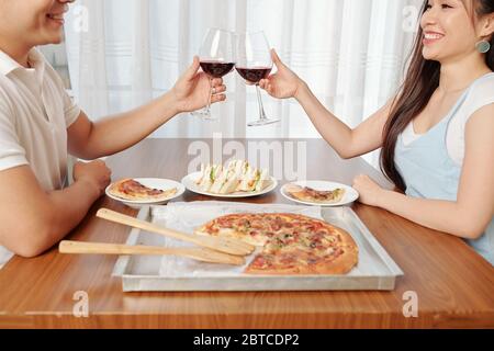 Happy young Vietnamese couple drinking red wine and eating pizza at home Stock Photo