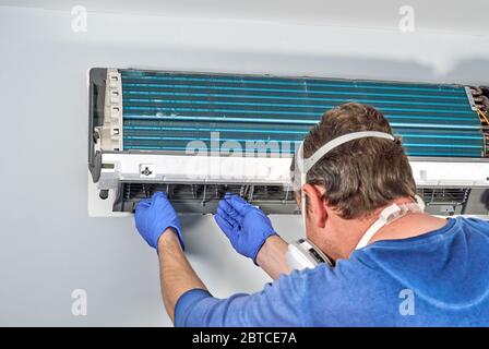 Technician in blue gloves and mask disassembling air conditioner and preparing it for cleaning. Cleaning air conditioners help to avoid growing mold w Stock Photo