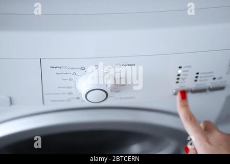 The girl sets the washing program for the washing machine Stock Photo