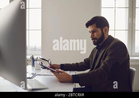 Businessman worker with a beard works in computer behind the workplace in the office. Stock Photo