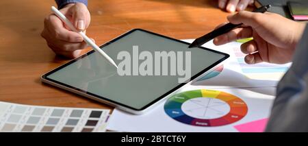 Cropped shot of two graphic designers working together with mock-up tablet and paperwork on wooden worktable Stock Photo