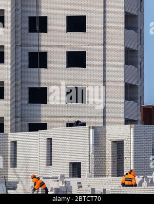 Construction site. Unfinished apartment building. Construction workers dressed in special clothing laying bricks. Stock Photo